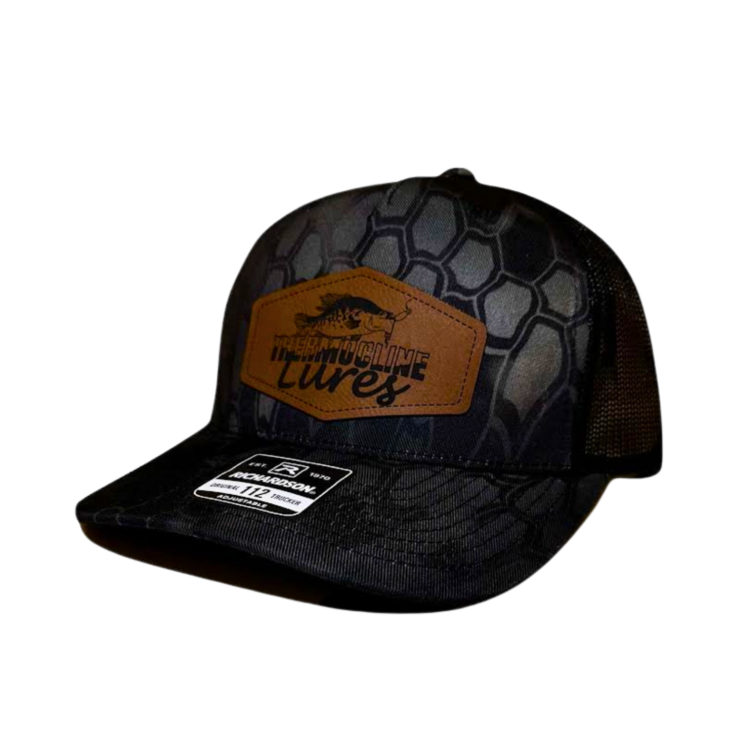 "Left side view of the Thermocline Lures Kryptek Typhon/Black Trucker Hat, featuring a leather patch logo with a crappie fish design, black hexagonal camo pattern on the front, and black mesh back panel.