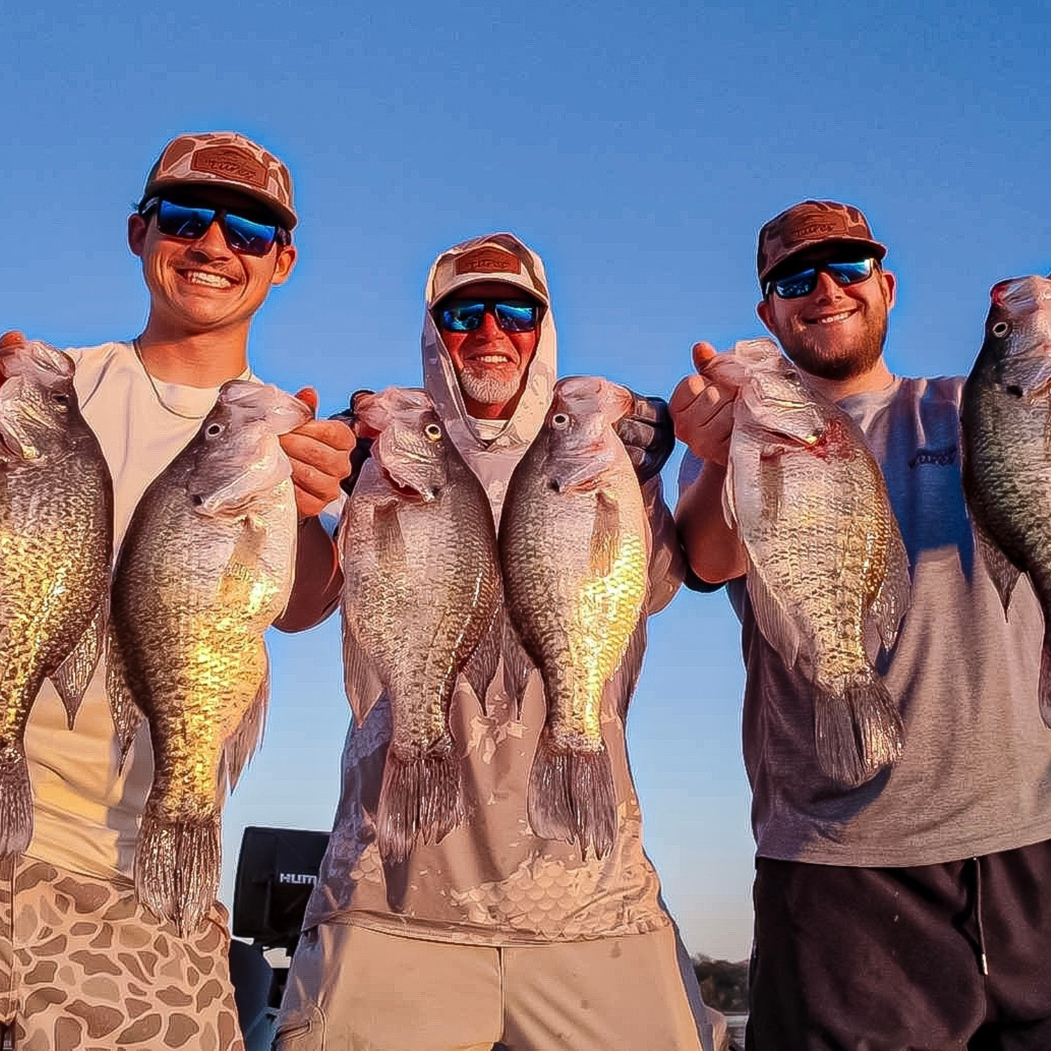Blake, Mason, and Tommy holding multiple crappie fish together as a team, smiling under a clear blue sky, showcasing Thermocline Lures gear.