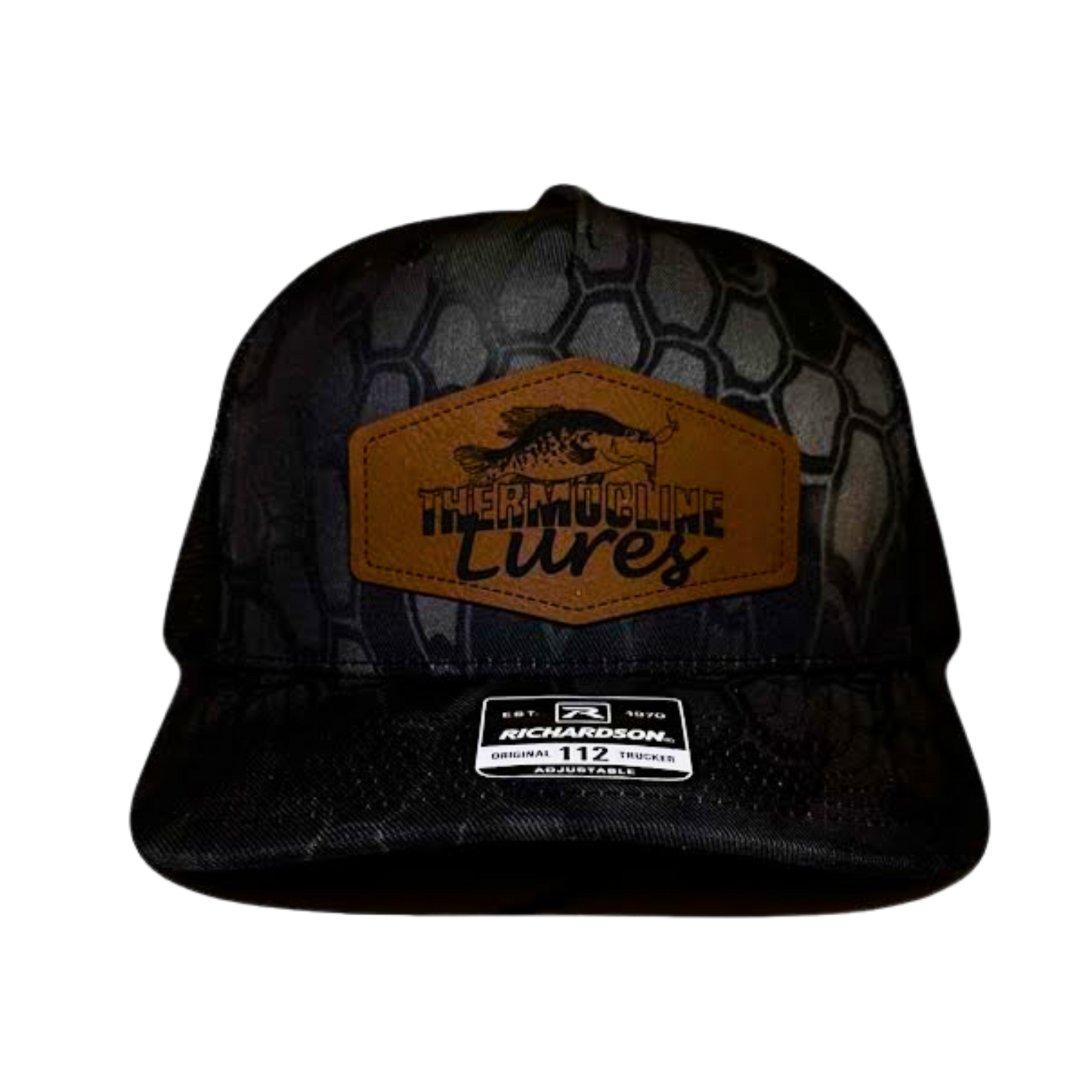 Front view of the Thermocline Lures Kryptek Typhon/Black Trucker Hat, showcasing a brown leather patch logo with a crappie fish design, a black hexagonal camo pattern, and a curved bill.