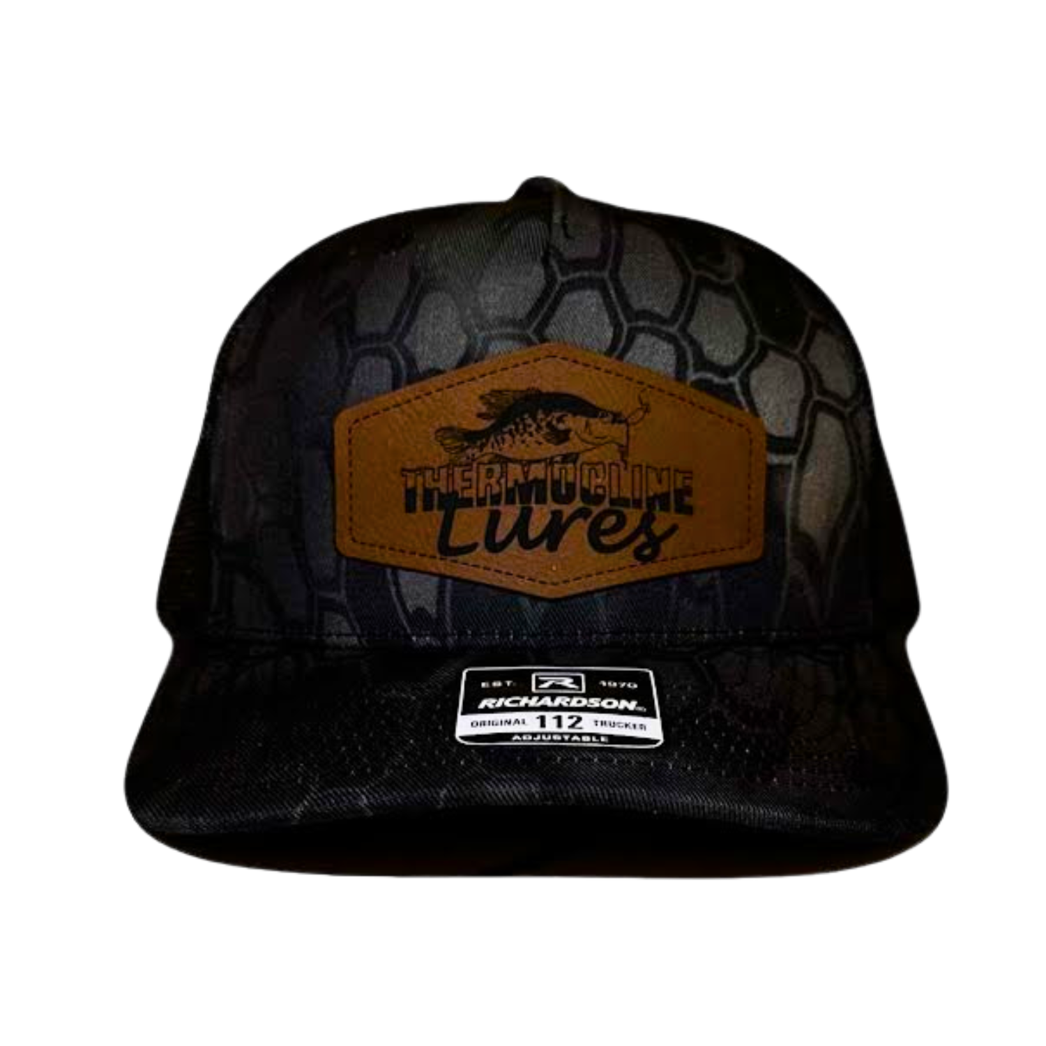 Front view of the Thermocline Lures Kryptek Typhon/Black Trucker Hat, showcasing a brown leather patch logo with a crappie fish design, a black hexagonal camo pattern, and a curved bill.