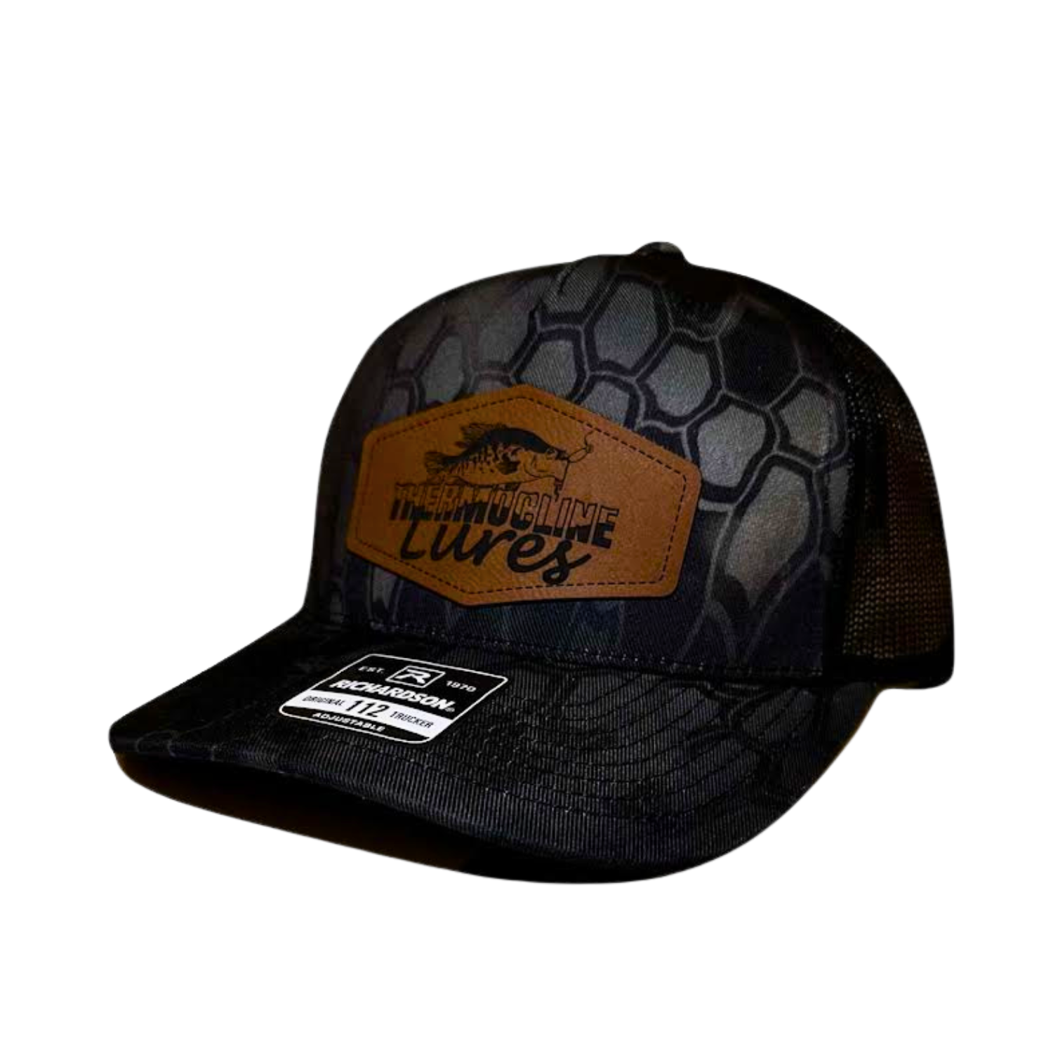 "Left side view of the Thermocline Lures Kryptek Typhon/Black Trucker Hat, featuring a leather patch logo with a crappie fish design, black hexagonal camo pattern on the front, and black mesh back panel.