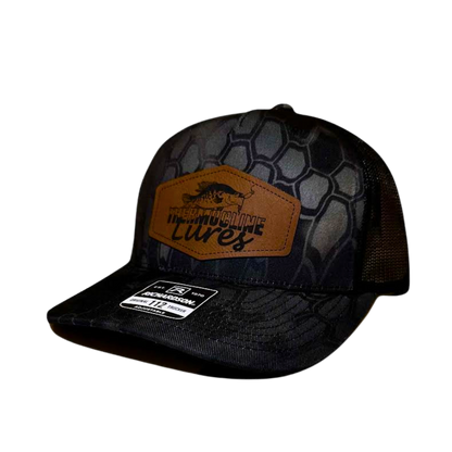 "Left side view of the Thermocline Lures Kryptek Typhon/Black Trucker Hat, featuring a leather patch logo with a crappie fish design, black hexagonal camo pattern on the front, and black mesh back panel.